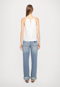 Weißes ärmelloses Top mit einer Schlüssel-Schlitzöffnung auf der Rückseite, kombiniert mit hochgeschnittenen, hellblauen Jeans aus Denim, die umgeschlagene Säume und Gesäßtaschen aufweisen.