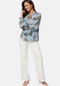 Light blue blouse with floral patterns, gathered neckline, and elastic cuffs, paired with white wide-legged pants and beige heels.