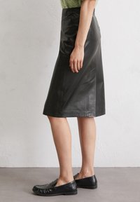 Schwarzer Leder A-Linien-Rock, knielang, mit glatter Textur und seitlichen Nahtdetails, kombiniert mit schwarzen Slippers.