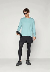 Šviesiai mėlyna ilgomis rankovėmis marškiniai, juodi šortai ir juodos pėdkelnės. Laikoma juoda vandens butelis. Juodi sportbačiai ir saulės akinių komplektas užbaigia įvaizdį.