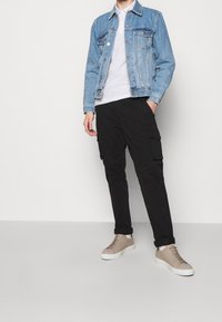 Světle modrá džínová bunda, bílá polo tričko, černé cargo kalhoty a béžové tenisky s texturovaným povrchem a tkaničkami. Jednoduchý, neformální outfit.
