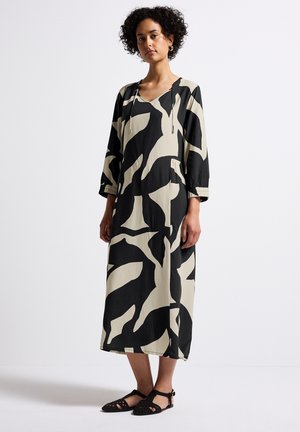 Robe longue et ample en noir et beige, ornée d'un motif abstrait, avec un décolleté en V et des manches trois-quarts. Portée avec des sandales plates noires.