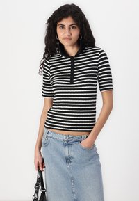 Svart-hvite stripete kortermet polo med ribbet tekstur og svart knappeplacket. Kombinert med et blått denim-skjørt.
