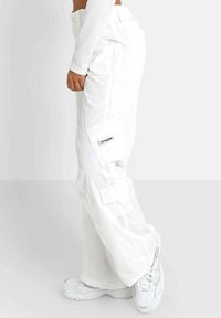 White cargo pants with side pockets, relaxed fit, and logo detail on the left pocket. Worn with white sneakers. Smooth texture.