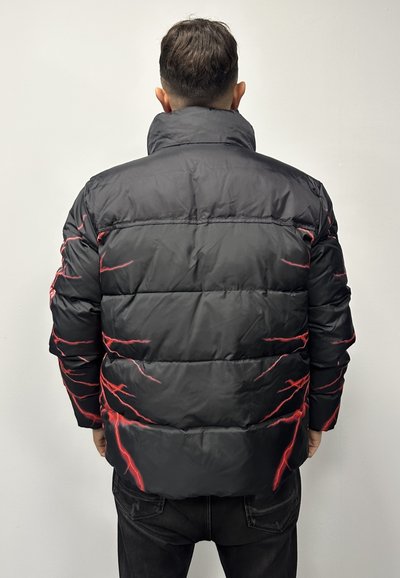 Giubbotto imbottito nero con motivi di fulmini rossi, colletto alto, design trapuntato e texture liscia, indossato con pantaloni neri.