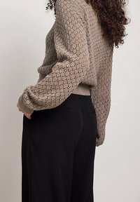 Knit-svikande i ljusbrunt med ett strukturerat diamantmönster, kombinerat med svarta byxor med sidofickor och en skräddarsydd passform.