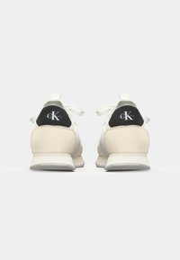 Adidași albaștri și bej cu un finisaj din piele texturată, având o tabulă pentru călcâi neagră cu un logo și șireturi plate, concepuți pentru confort.