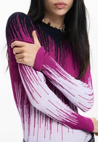 Kötött pulóver, amelynek színátmenetes mintája fekete, rózsaszín és fehér között váltakozik. Hosszú ujjakkal és bordázott mandzsettákkal rendelkezik. Sima textúra.