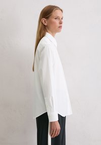 Biała koszula na guziki z klasycznym kołnierzykiem, z długimi rękawami, luźnym krojem i gładką bawełnianą fakturą.