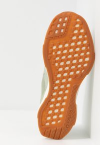 Sole boty Reebok s texturovanou oranžovou gumou a mřížkovaným vzorem, doplněná světle zeleným svrškem a bílými akcenty na mezipodešvi.