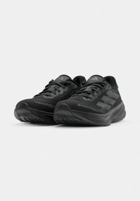 Paar schwarze athletische Laufschuhe mit strukturierten Sohlen und Schnürsenkeln, nach vorne geneigt auf einfarbigem hellgrauem Hintergrund.