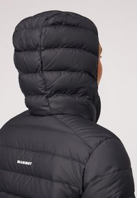 Svart pufferjacka med huva, med horisontella kviltade sektioner och en vit logotyp på baksidan. Slät, matt yta.