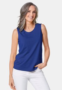 Ärmelloses blaues Top aus glattem Stoff mit rundem Ausschnitt, kombiniert mit weißen Hosen. Das Kleidungsstück hat eine lässige Passform und ein minimales Design.