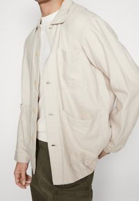 Lichtbeige button-up jack gemaakt van zachte, gestructureerde stof. Voorzien van een kraag, twee voorzakken en subtiele stikdetails.
