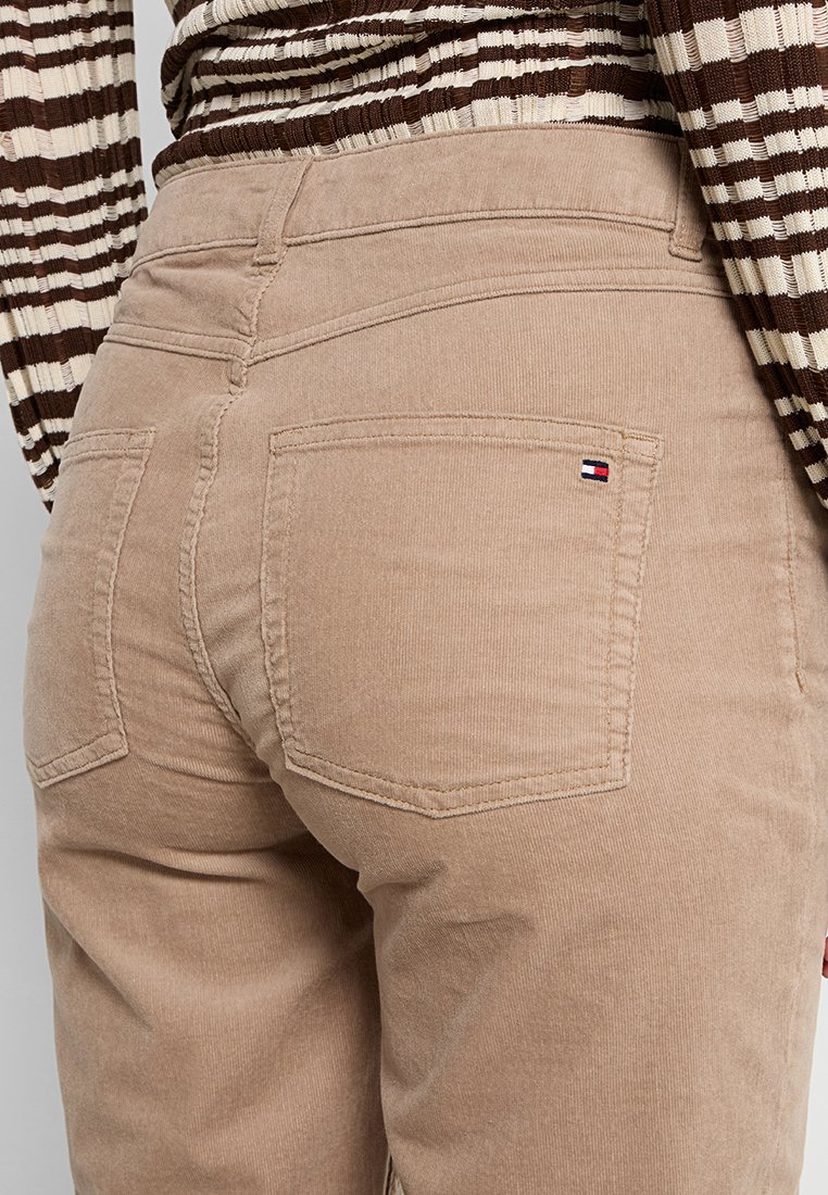 Beige Corduroy-Hose mit tailliertem Design, zwei Gesäßtaschen und einem kleinen Logotag an der rechten Tasche. Strukturierte Oberfläche über die gesamte Hose.
