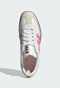 Sneaker in pelle bianca con accenti beige chiaro, con tre strisce rosa, lacci bianchi piatti e una linguetta imbottita con stampa del logo sulla soletta.
