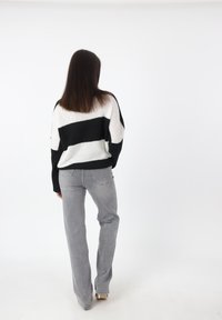 Maglione a righe bianche e nere con vestibilità comoda, abbinato a jeans dritti grigi. Materiale a maglia morbido; sfondo semplice.