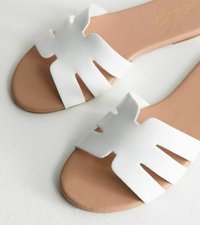 Sandalias deslizantes blancas con un diseño recortado, que cuentan con un acabado suave y una plantilla de color marrón. La suela es plana y texturizada para un mejor agarre.