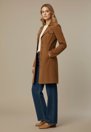 Brauner Cordmantel mit figurbetonter Silhouette, großen Knöpfen und Pattentaschen, kombiniert mit weitem, blauen Jeans und hellbraunen Loafers.