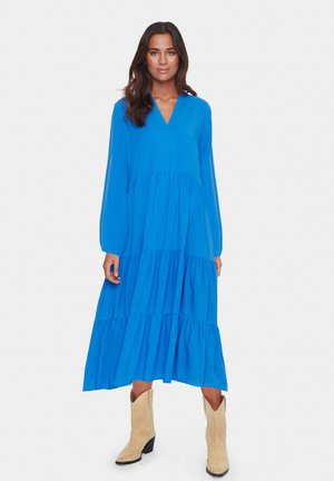 Rochie midi albastră cu fuste înclinate, cu mâneci lungi, decolteu în V și material fluid. Cefele de jos au multiple straturi volăte.