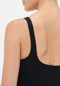 Woman's upper back and shoulder with black tank top strap against plain white background.