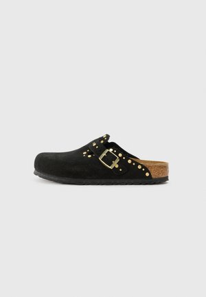 Zoccolo in suede nero con punta rotonda, suola in sughero, borchie dorate e dettaglio con fibbia, e design senza retro per una facile vestibilità.