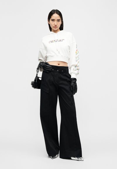 Λευκή cropped φούτερ με πολύχρωμη γραφική λεπτομέρεια στα μανίκια, συνδυασμένη με μαύρο παντελόνι ψηλόμεσο, φαρδύ και μαύρα γάντια. Μαύρη τσάντα χειρός.