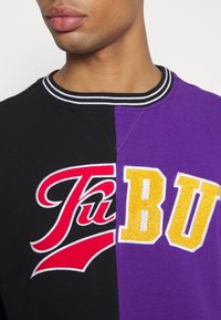 Czarna i fioletowa bluza z okrągłym dekoltem z wyszywanym czerwonym logo "FUBU" oraz żółtymi literami "BU", ze ściągaczem w paski przy kołnierzu.