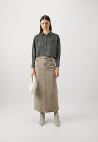 Camisa cinza cortada com um bolso frontal, saia de ganga bege e botas cinzentas claras até ao tornozelo. Segurando uma bolsa branca. Design simples com texturas suaves.
