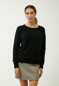 Maglione nero e morbido con scollatura rotonda e maniche lunghe, abbinato a una mini gonna a trama e motivo. Design semplice e minimalista.