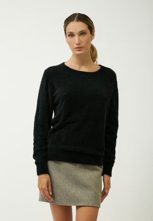 Schwarzer, flauschiger Pullover mit rundem Ausschnitt und langen Ärmeln, kombiniert mit einem strukturierten, gemusterten Minirock. Einfaches, minimalistisches Design.