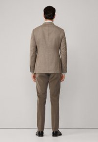 Hellbrauner, taillierter Blazer mit strukturierter Oberfläche, kombiniert mit beigen Hosen. Der Rücken verfügt über einen einzelnen Schlitz und subtile Schulterformen.