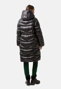 Black puffer coat with a hood, featuring a quilted chevron design and shiny finish. Worn over green pants and black boots.