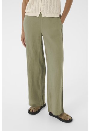 Pantalons en lin vert olive légers avec une coupe ample ; dotés de poches latérales et d'un design à jambe droite, associés à des sandales à brides sombres.