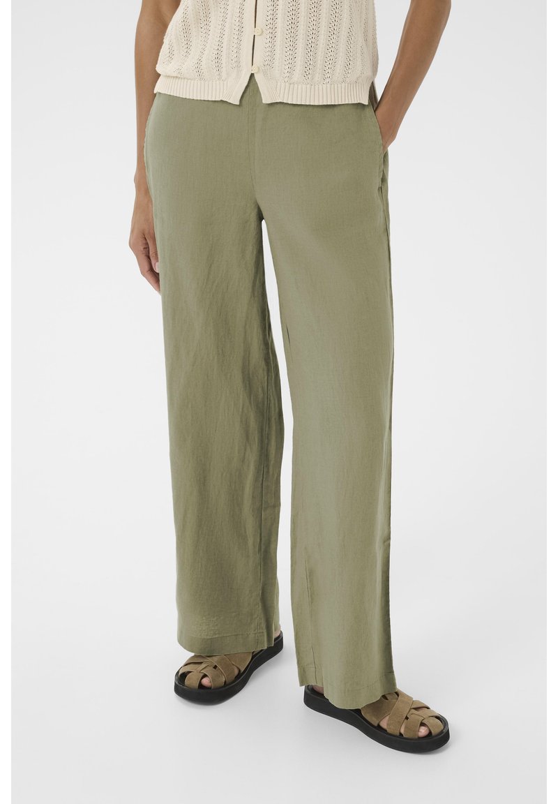 Lichte, olijfgroene linnen broek met een loose fit; heeft zijzakken en een rechte pijpdesign, gecombineerd met donkere bandensandalen.