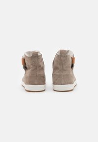 Cizme de gleznă din suede maro cu o talpă albă, având un accent din piele bej și un tab pentru tragere în spate. Textură moale și design simplu.