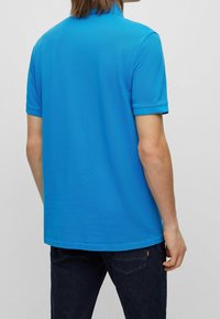 Polotröja i klarblått, tillverkad av en strukturerad tyg, har en klassisk krage och korta ärmar. Bärs med mörkblå jeans.