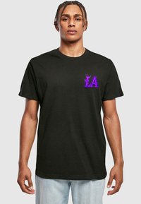 Svart T-skjorte med kort arm laget av bomull, med en lilla flamme-design med "LA" på venstre brystområde. Klassisk rund hals stil.
