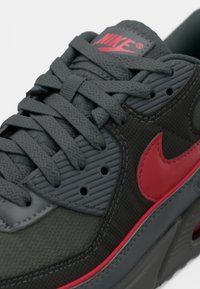 Krupan plan tamnosivih Nike tenisica s koraljno ružičastim Swoosh logom, teksturiranim vezicama i podstavljenim jezikom.