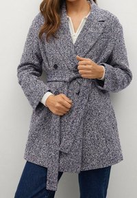 Cappotto a scacchi navy e bianco con vita regolabile, caratterizzato da un design doppiopetto e grandi bottoni frontali.