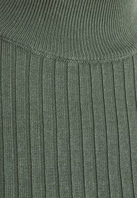 Tissu en maille côtelée de couleur vert foncé, présentant des rayures verticales. La texture est douce avec un aspect légèrement extensible.