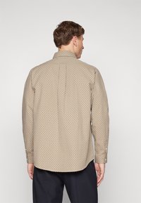 Beige színű, hosszú ujjú ing, kicsi geometrikus mintával. Gombos gallérral és mandzsettával rendelkezik, kerekített alsó résszel és laza szabással.