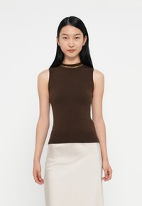 Bruine mouwloze top met een hoge halslijn, voorzien van een gouden kettingaccent rond de kraag, gedragen met een lichte satijnen rok.