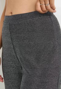 Leggings noirs texturés avec une large taille. Le matériau a une légère brillance. Gros plan montrant le détail de la couture latérale et la finition lisse.