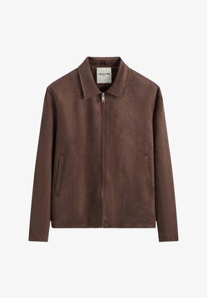 Veste zippée en daim marron avec col pointu et deux poches latérales, présentée sur fond blanc.