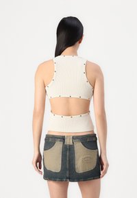 Top corto a coste in bianco sporco con borchie argentate lungo i fori per le braccia, abbinato a una gonna in denim scuro con tasche a contrasto.