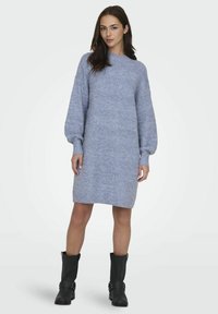 Strikket kjole i lys blå med et teksturert mønster, rund halslinning og lange puffermer, sammen med svarte ankelstøvletter.