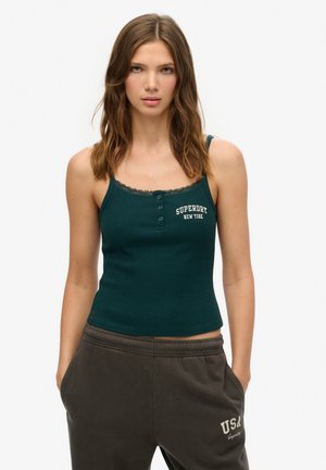 Camiseta de tirantes verde azulado con ribete de encaje, que presenta cuatro botones y la impresión "Superdry New York". Combinada con pantalones de chándal gris oscuro.