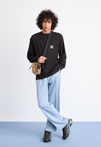 Black long-sleeve shirt with a pocket, light blue wide-leg pants, and black sneakers. Small bag slung across body. Smooth fabric texture.