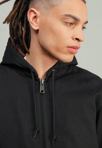 Black zip-up hoodie with drawstrings, featuring a smooth texture and a minimalist design. Silver zipper and hood complete the look.